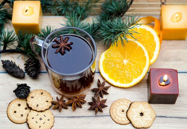 Glass of tea or vine and rounded chrismas cookie. Pine branch with spice star anise and orange slice arranged on wooden table.Winter and autumn healthy snack