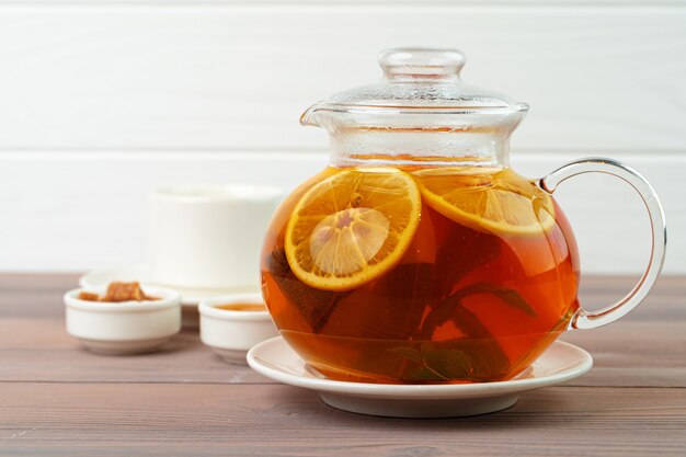 Glass teapot with black tea and pieces of citrus close up