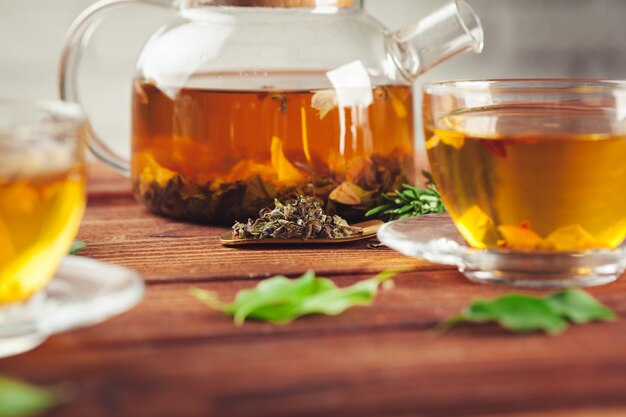 Glass teapot with cup of black tea on wooden table