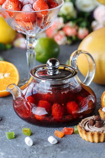 Glass teapot with fruit raspberry tea and mint on a blue table with fruits and decorations