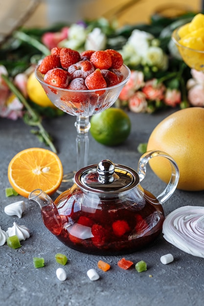 Glass teapot with fruit raspberry tea and mint on a blue table with fruits and decorations