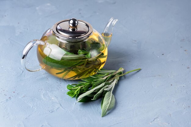 Glass Teapot with Herbal Tea Hot and Tasty Tea with Mint Sage and Rosemary Blue Background Copy Space