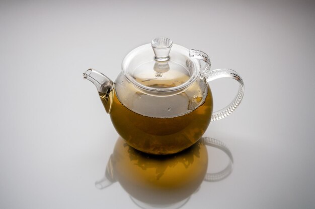 Glass teapot with herbal tea reflected on white background