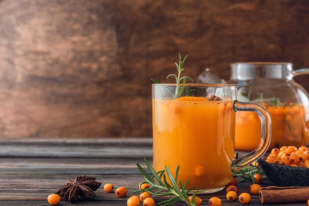 Glass and teapot with hot autumn drink Sea buckthorn tea with orange cinnamon and rosemary on wooden table