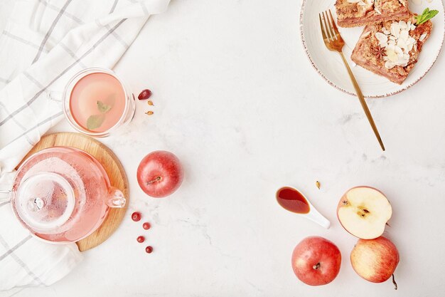 Glass teapot with natural cranberry tea and slices of homemade apple pie with almond flakes and apples Copy space