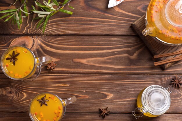 Glass teapot with orange sea buckthorn tea. Hot winter drinks on brown wooden background.