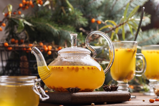 Glass teapot with orange sea buckthorn tea. Hot winter drinks on brown wooden table