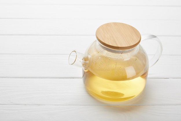 Glass teapot with organic herbal tea on white wooden table with copy space