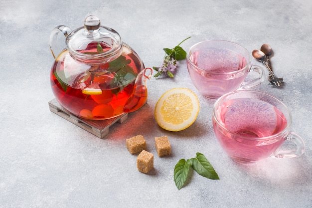 Glass teapot with tea, mint and lemon on grey table