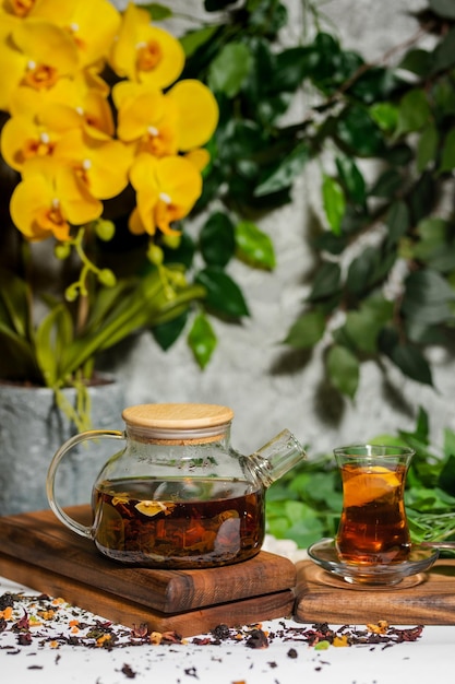 A glass teapot with a yellow flower in the background