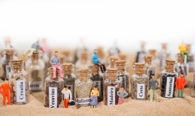 Фото Стеклянная пробирка с песком различных мест летнего отдыха. расположенный в песке с маленькими фигурами людей.