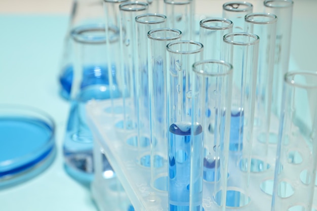 Glass test tubes and flasks with liquid on blue background close up