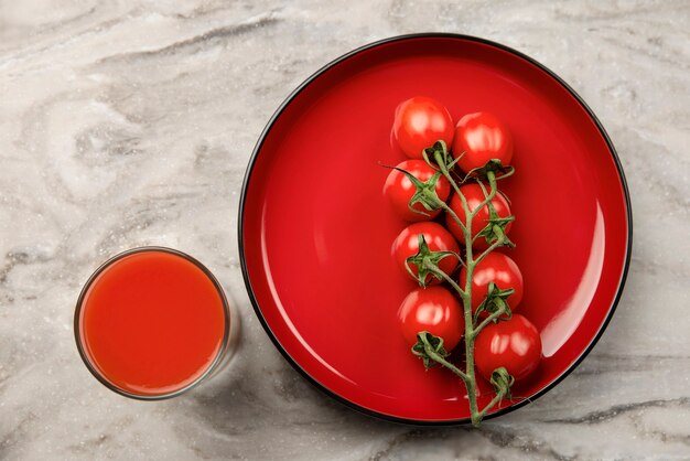 A glass of tomato juice and a branch of small tomatoes banner cherry tomatoes in a red plate