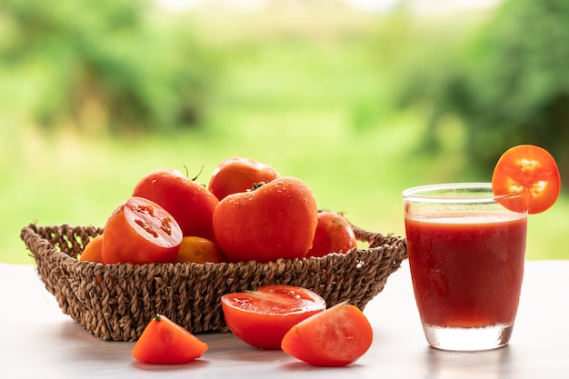 トマトジュースと緑の自然の背景と大理石のテーブルに新鮮なトマトのガラス。