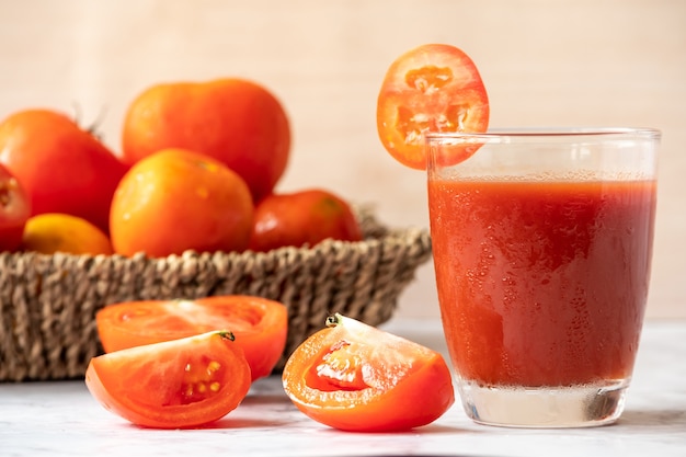 Glass of tomato juice and fresh tomatoes on marble table. 