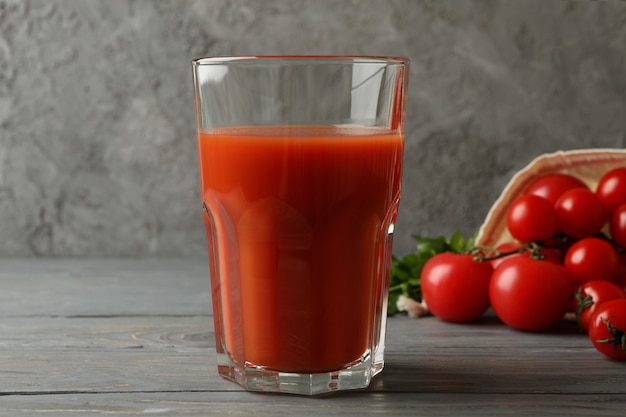 Glass of tomato juice and tomatoes on gray wooden table