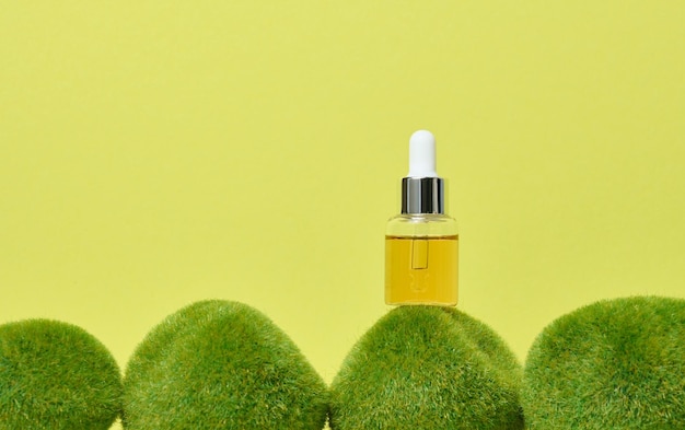 Glass transparent bottle with pipette and yellow oil on green moss