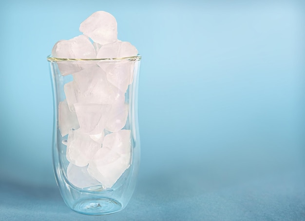 A glass transparent cup with ice stands on a textured blue background