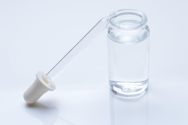 Glass transparent jar and a cosmetic pipette with liquid droplets on a white background.