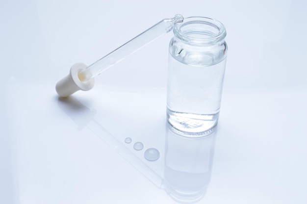 ガラスの透明な瓶と白い背景の上の液滴と化粧品のピペット