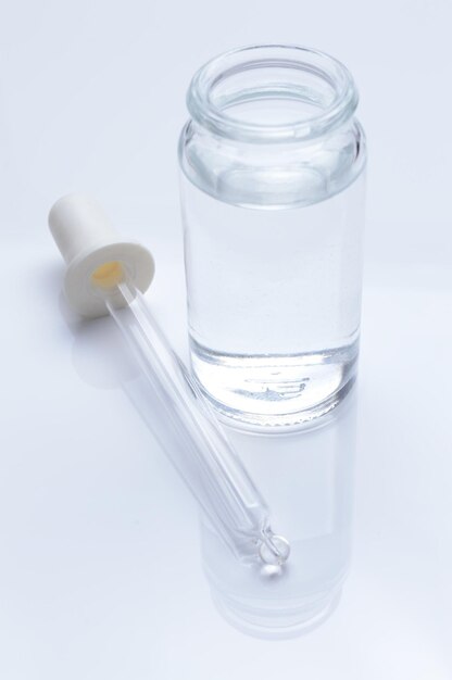 glass transparent jar and a cosmetic pipette with liquid droplets on a white background