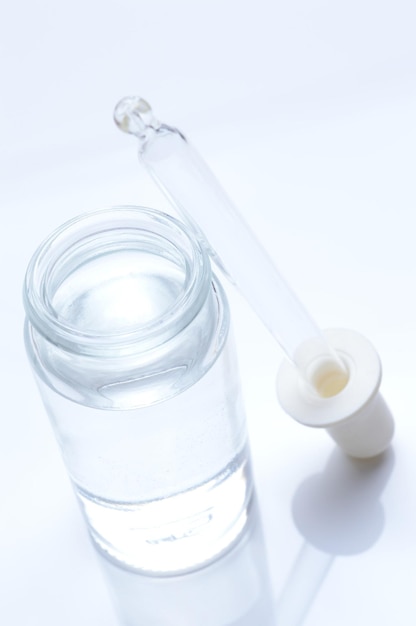 glass transparent jar and a cosmetic pipette with liquid droplets on a white background