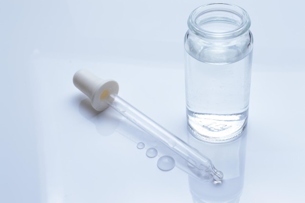 glass transparent jar and a cosmetic pipette with liquid droplets on a white background