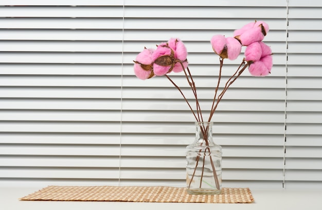 Glass transparent vase with a bouquet of pink cotton flowers on\
a white table