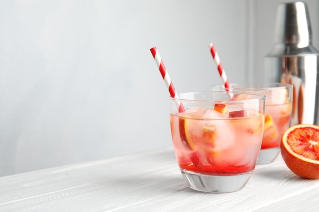 Glass of tropical cocktail with ice cubes on table against light background Space for text