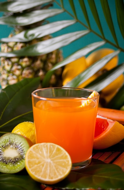 Glass of tropical exotic multifruit juice with pineapple, fruits and palm leaf 