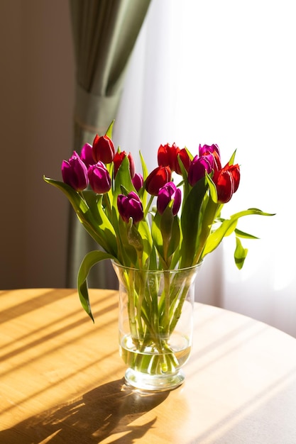 Glass vase on the table with tulips light from the window and shadows Place for text romantic