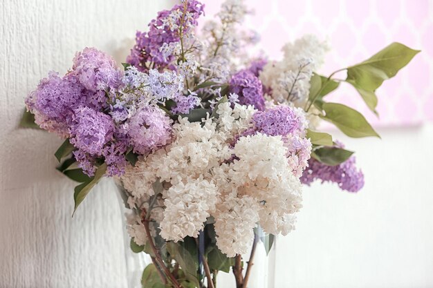 写真 明るい壁の背景に美しいライラック色の花を持つガラスの花瓶