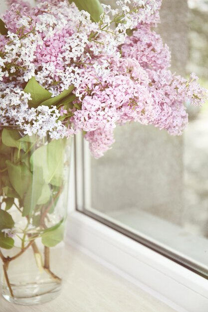 Photo glass vase with beautiful lilac flowers on window sill