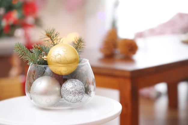 Стеклянная ваза с ветками и рождественскими шарами на размытом фоне