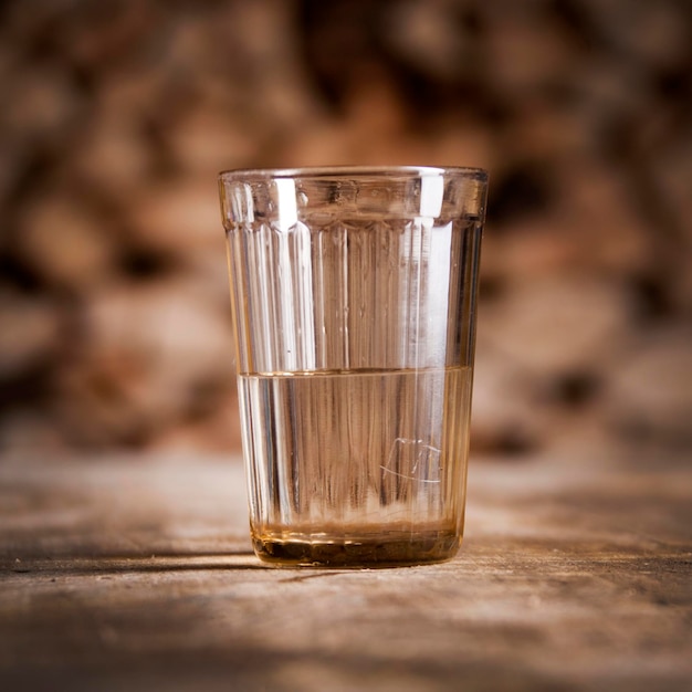 A glass of vodka on a wooden table and firewood behind