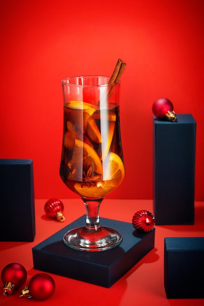 Glass of warm homemade mulled wine made with sliced oranges, cinnamon stick and spices on red