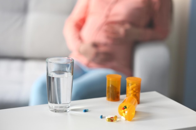 Glass of water and bottles with medicines against pregnant woman background