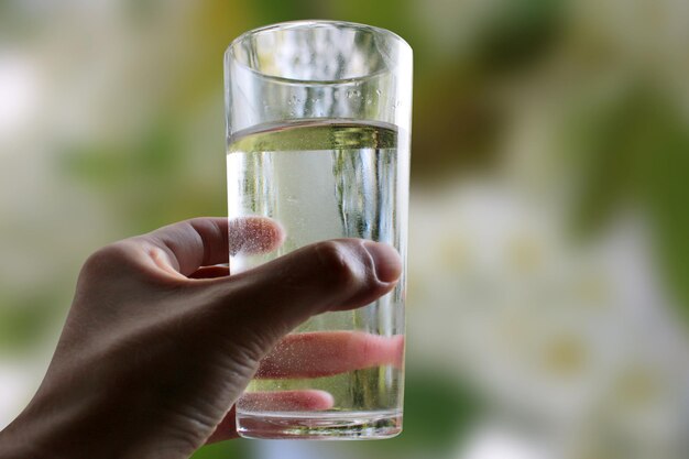 Un bicchiere d'acqua in un primo piano della mano su uno sfondo verde naturale all'aperto