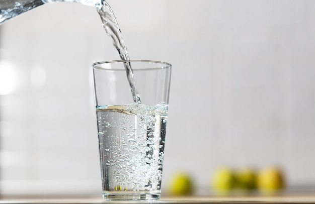 Glass of water is poured from the jug into a single glass in a kitchen table