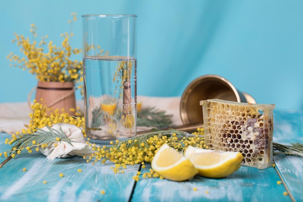 Glass of water, mimosa flowers, honeycomb and pieces of lemon on a wooden surface. Closeup