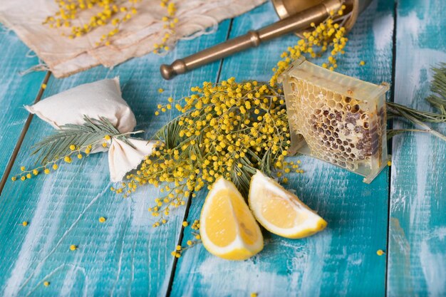 Glass of water, mimosa flowers, honeycomb and pieces of lemon on a wooden surface. Closeup