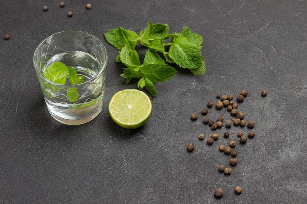 Glass of water and mint. Half lime and sprigs of mint on table. Black background. Top view.