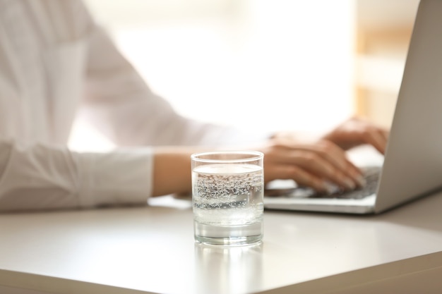 Photo glass of water near woman working on laptop at table