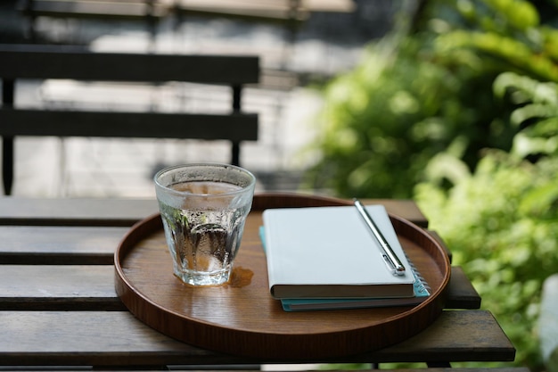 glass of water and notebooks on wooden tray