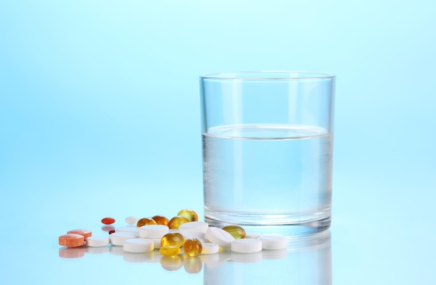 Glass of water and pills on blue background