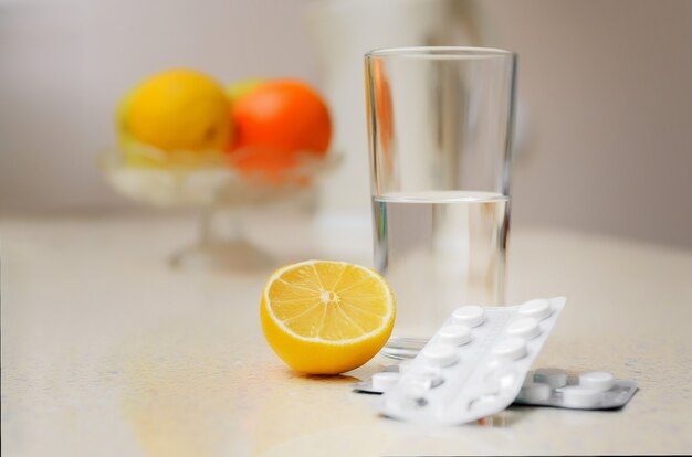 A glass of water, pills for the disease and a lemon stand on the table against the background of fruit