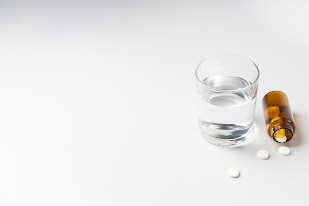 Glass of water and pills from a jar on a white background