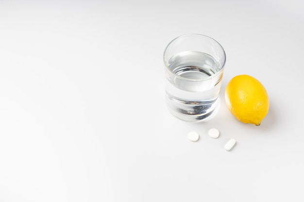 Glass of water, pills and lemon on a white background