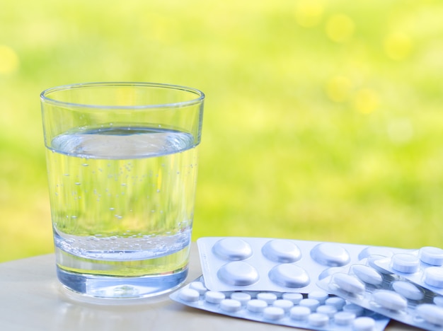 水と緑の自然の背景にテーブルの上の丸薬のガラス。花や花粉にアレルギー