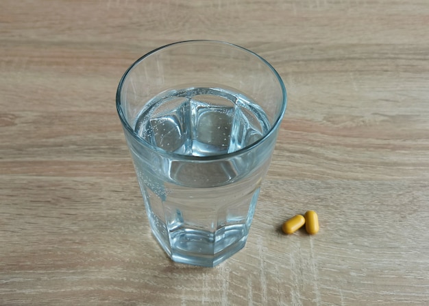 Bicchiere d'acqua e pillole su un tavolo di legno
